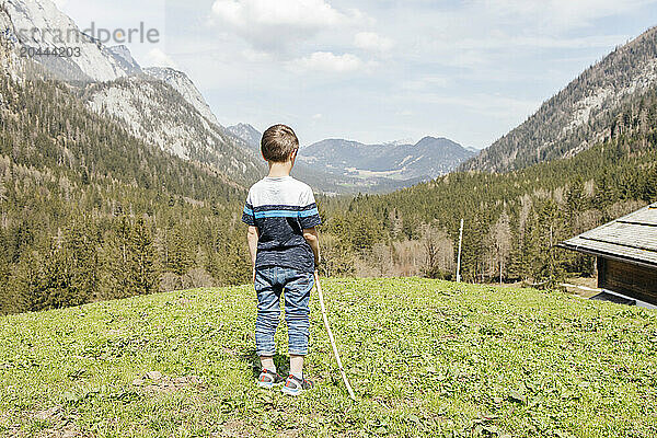 Boy standing with stick in front of mountains