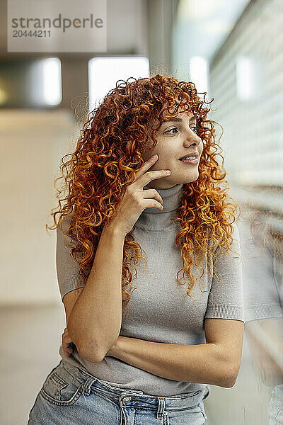 Smiling redhead young woman looking out through window