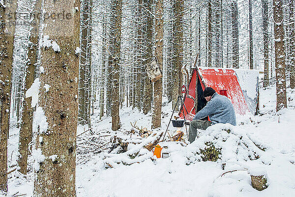 Senior man enjoying bonfire in snow near tent at forest