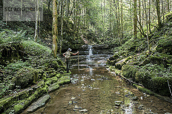 Senior man standing near water stream in forest