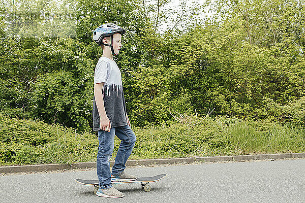 Boy wearing cycling helmet standing with skateboard on road