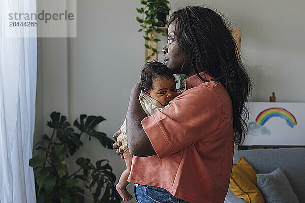 Thoughtful mother embracing daughter and standing at home