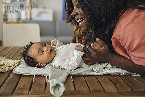 Playful mother playing with daughter lying on wooden table at home