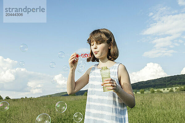 Cute young girl blowing soap bubbles at field on sunny day