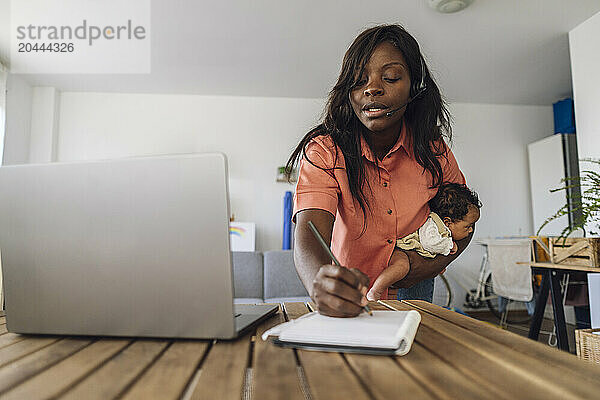 Freelance woman carrying daughter and writing in diary working at home