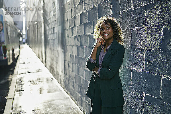 Smiling beautiful young businesswoman standing in front of wall