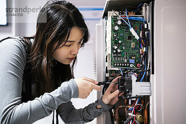 Young technician repairing air conditioner with tool