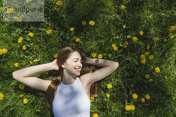 Happy teenage girl lying on yellow dandelions in park