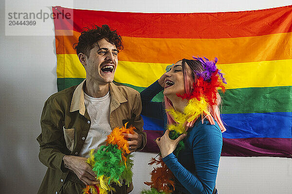 Cheerful friends enjoying pride party near rainbow flag at home