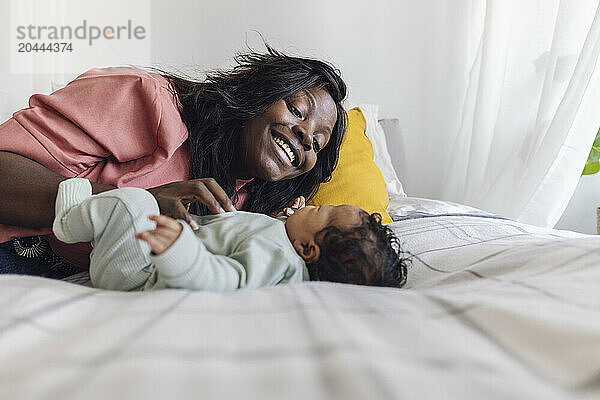 Happy mother playing with daughter lying on bed at home