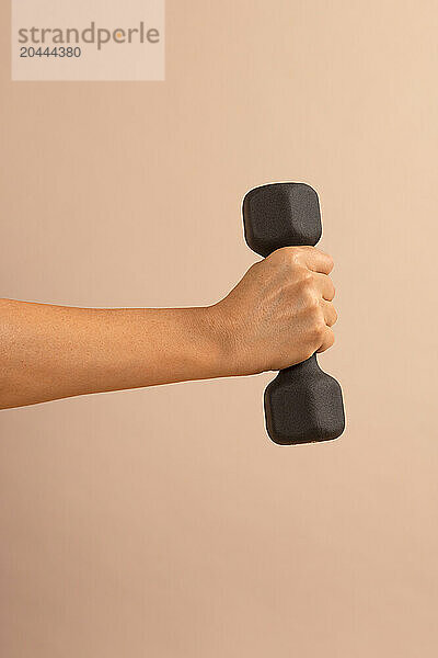 Hand of woman holding dumbbell against colored background