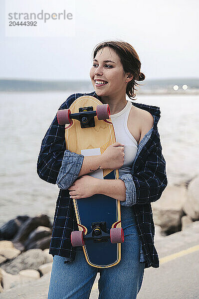 Happy young woman embracing skateboard