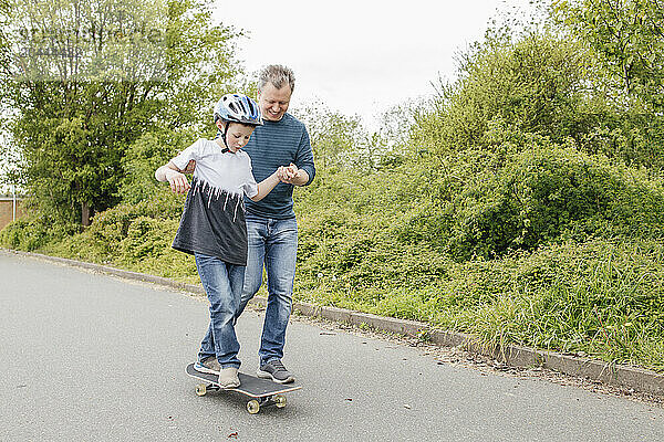 Father teaching son skateboarding on road