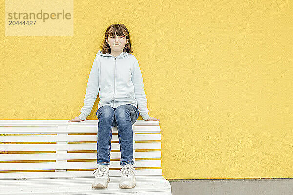 Girl sitting on bench in front of yellow wall