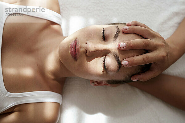 Hands of mature physiotherapist massaging teenage patient's head in hospital