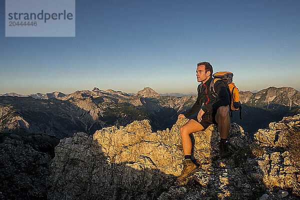 Man sitting on Steinfeldspitze rock at sunrise in Altenmarkt  Zauchensee  Salzburg  Austria