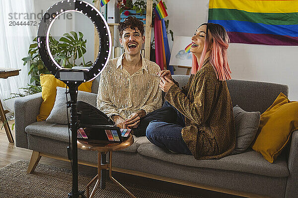 Cheerful non-binary person preparing for pride party and vlogging with friend at home