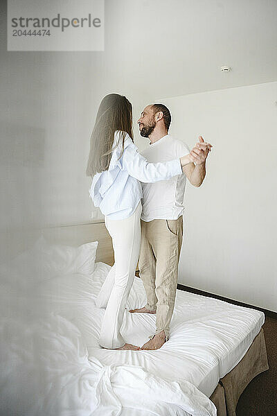 Couple holding hands and dancing on bed at home