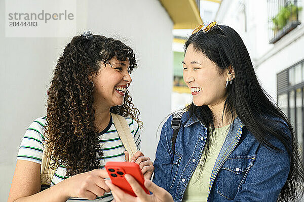 Woman holding smartphone and laughing with friend