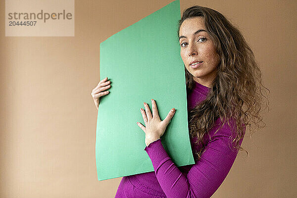 Woman holding green paper against beige background