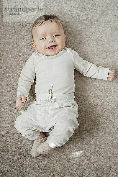 Smiling baby boy lying on beige blanket