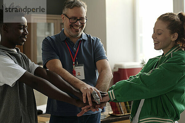 Happy coach encouraging students by stacking hands and cheering for baseball game at university