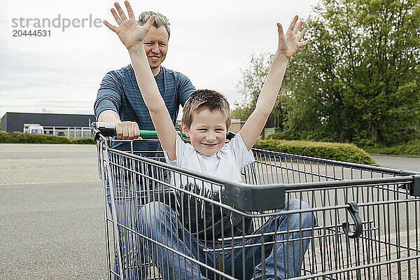 Father pushing son sitting in shopping cart at sidewalk