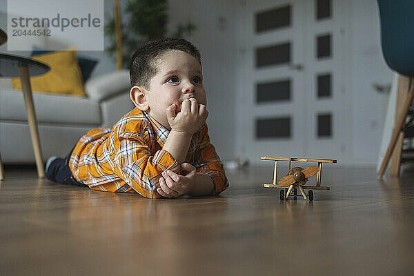 Boy lying on floor near toy airplane and watching TV at home