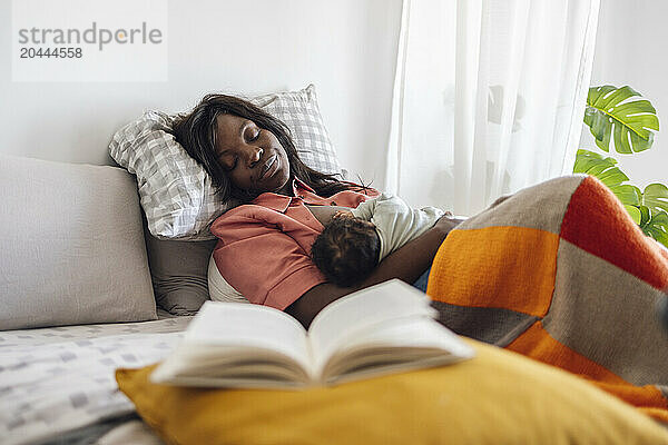 Tired mother breastfeeding daughter and lying on bed at home