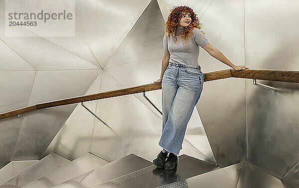 Beautiful redhead young woman leaning on railing at illuminated staircase