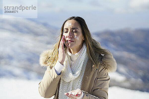 Woman with eyes closed applying sunscreen in winter