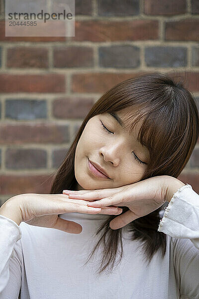 Smiling beautiful woman with eyes closed in front of brick wall