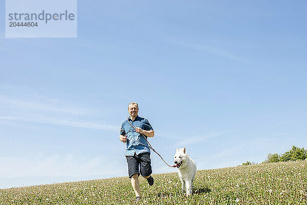 Man running with white Swiss shepherd dog in field