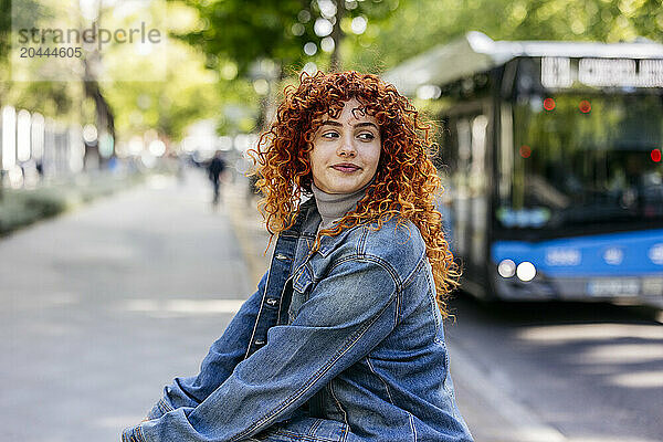 Beautiful redhead young woman with curly hair sitting at sidewalk