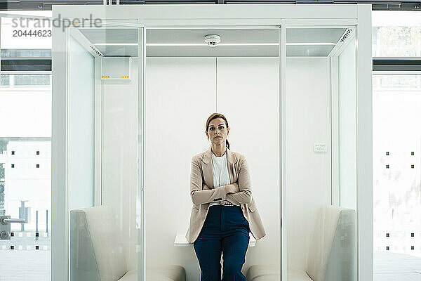 Businesswoman leaning on table with arms crossed at office