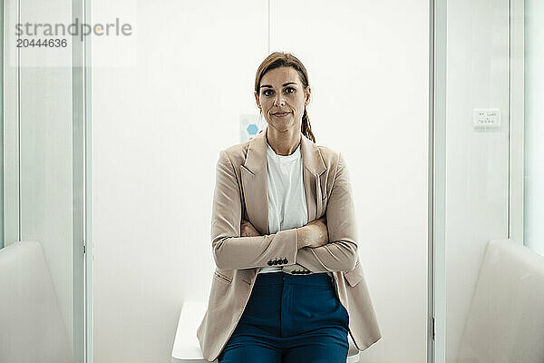 Smiling businesswoman with arms crossed leaning on table at office