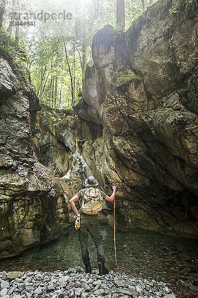 Senior man standing with hiking pole near lake in front of rocks