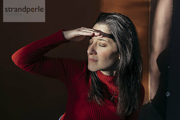 Woman shielding eyes with hand near wall