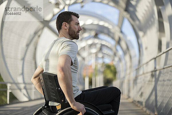 Man with disability sitting on wheelchair at bridge