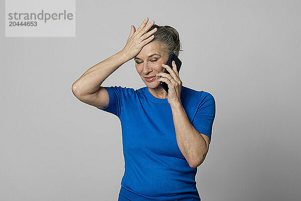 Senior woman with head in hand talking on mobile phone