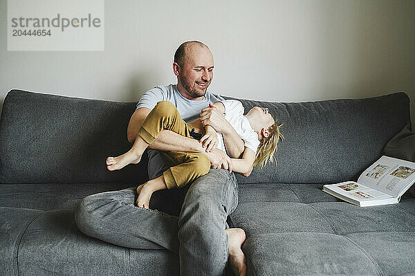 Father tickling son sitting on sofa at home