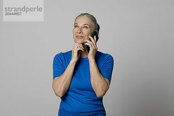 Senior woman talking on smart phone in front of wall