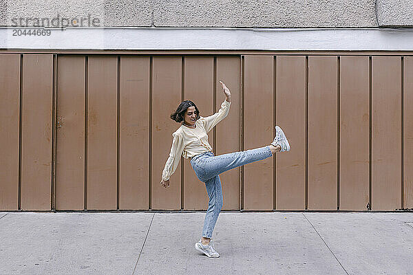 Happy woman dancing and enjoying in front of brown wall