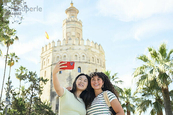 Smiling friends taking selfie through smartphone in front of Torre del Oro