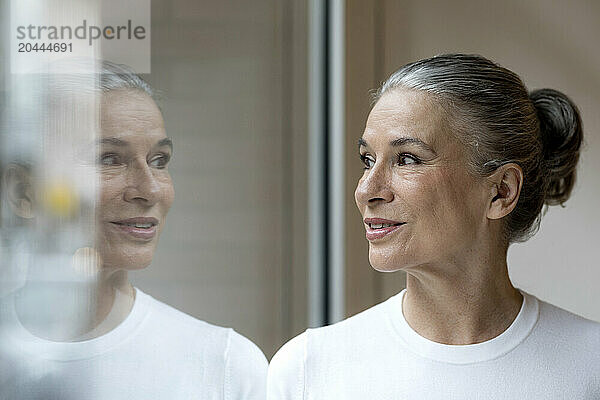 Smiling senior gray haired woman looking out through window