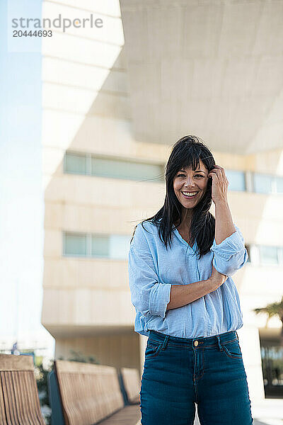 Happy businesswoman with hand in hair in front of building