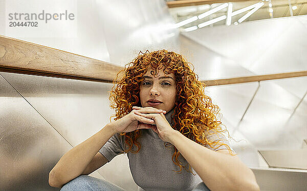 Beautiful redhead young woman with curly hair sitting on staircase