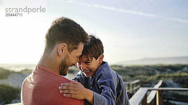 Playful father and son face to face spending leisure time at beach