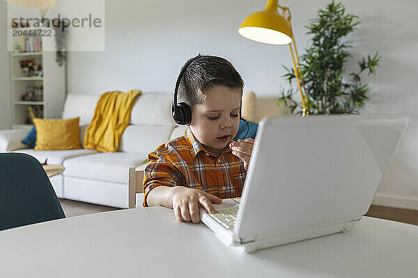 Boy sitting with laptop and talking on headset microphone at home