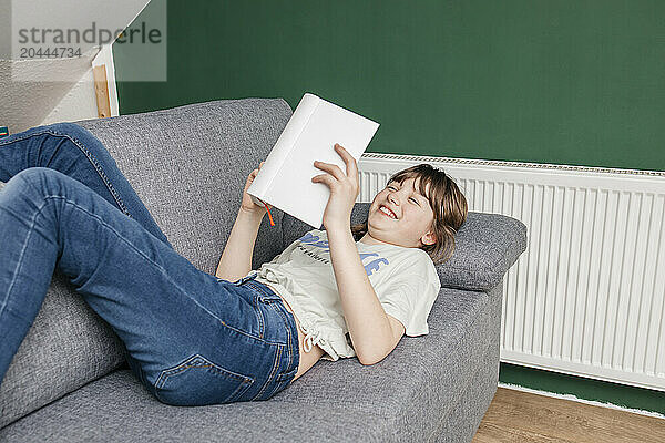 Teenage girl reading book lying on sofa